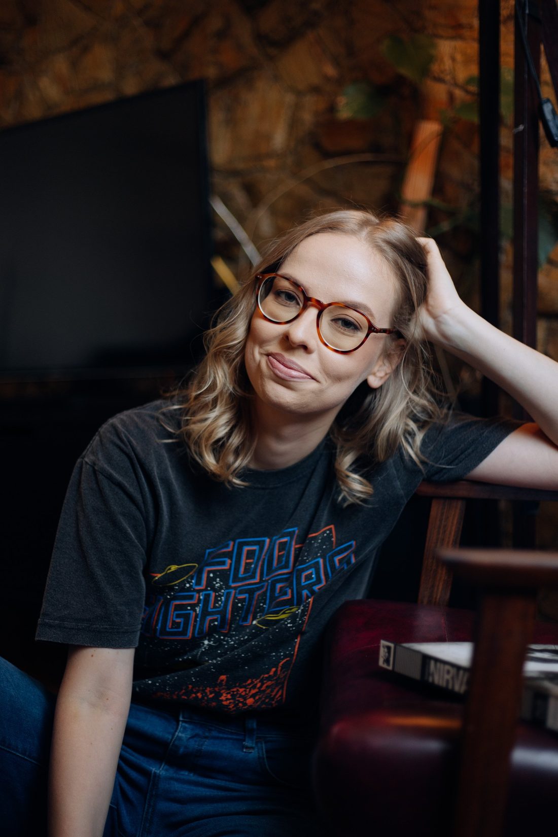 Júlia de Andrade sitting, leaning on the back of an armchair, looking at the camera.